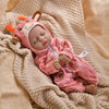 A pink animal romper set for a baby doll lying on a beige knitted fabric.