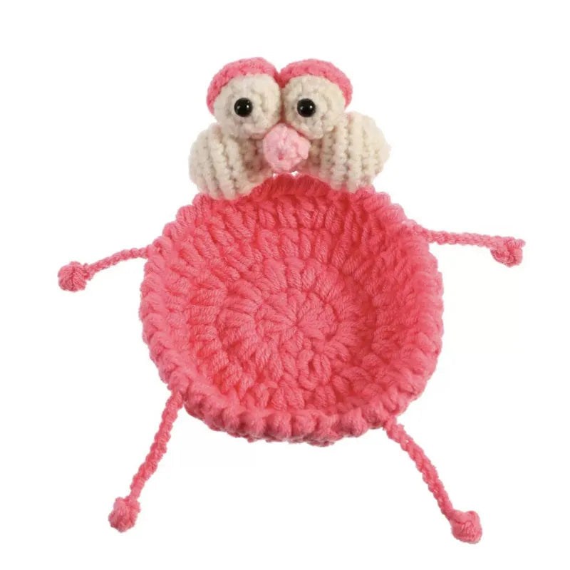A handmade crochet lizard with large eyes sitting on a pink circular coaster.