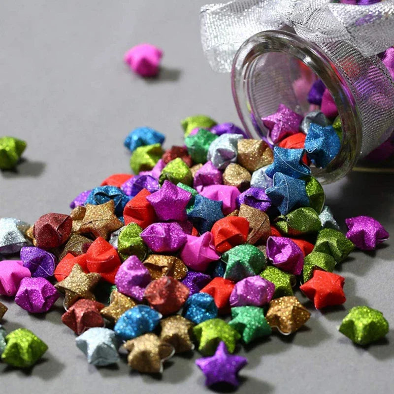 A pile of colorful glitter origami star paper strips in various shades and colors, with a glass jar visible.