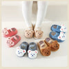 A set of adorable cartoon bear baby booties in pink and blue, shown with a baby wearing white socks.