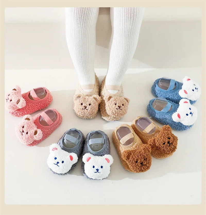 A set of adorable cartoon bear baby booties in pink and blue, shown with a baby wearing white socks.