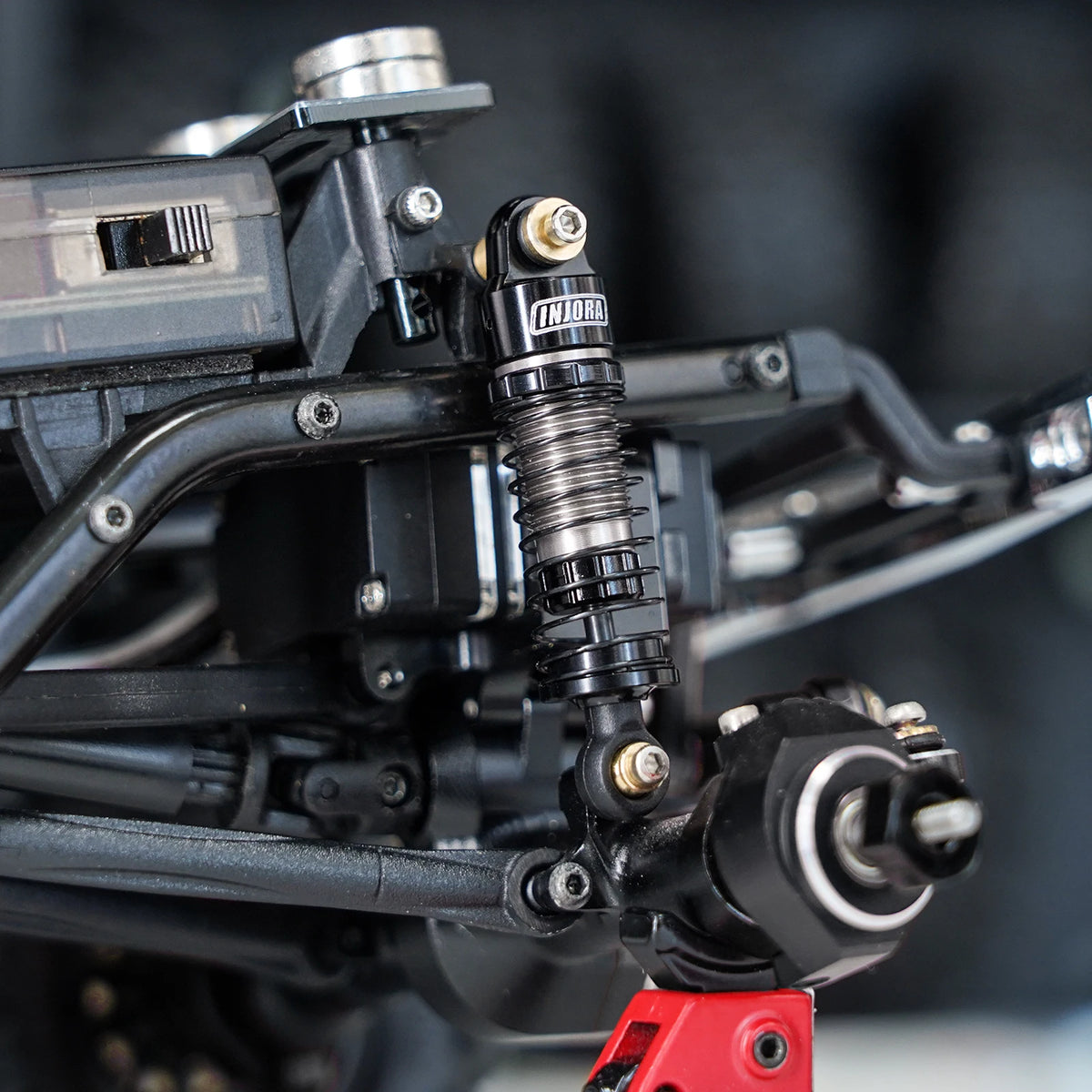 Close-up of heavy-duty oil shocks for 1/24 RC crawlers mounted on a black chassis.