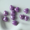 A collection of small, heart-shaped purple ceramic beads scattered on a white surface.