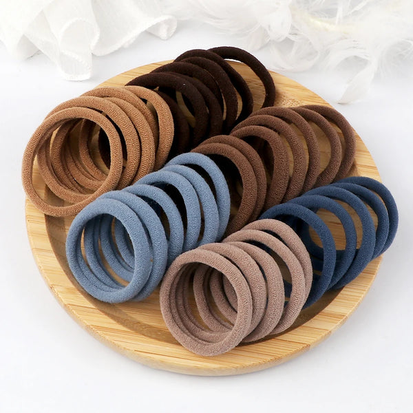 A wooden plate holds a stack of 50 elastic hair bands in various earth tones like brown, tan, and blue.
