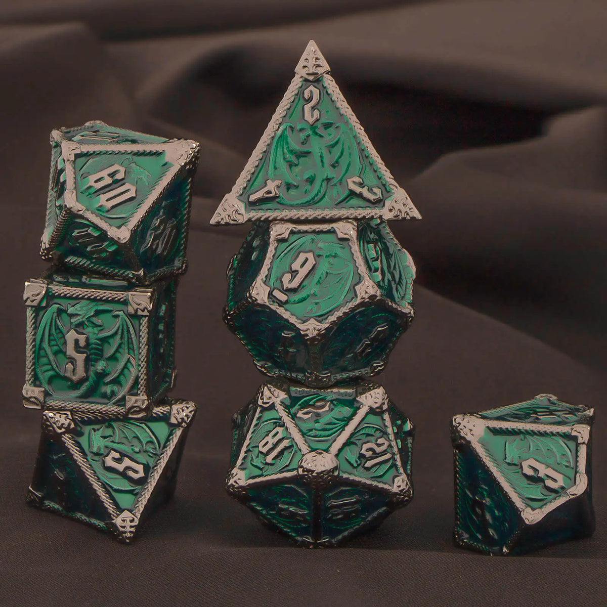 A set of seven polyhedral metal dice in teal and silver resting on a dark gray fabric.