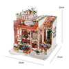 A detailed miniature dollhouse kit featuring a house, furniture, plants, and warm lighting elements.