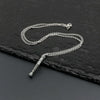 A silver mini metal saber chain necklace with a bail and a small pendant resting on a dark surface.