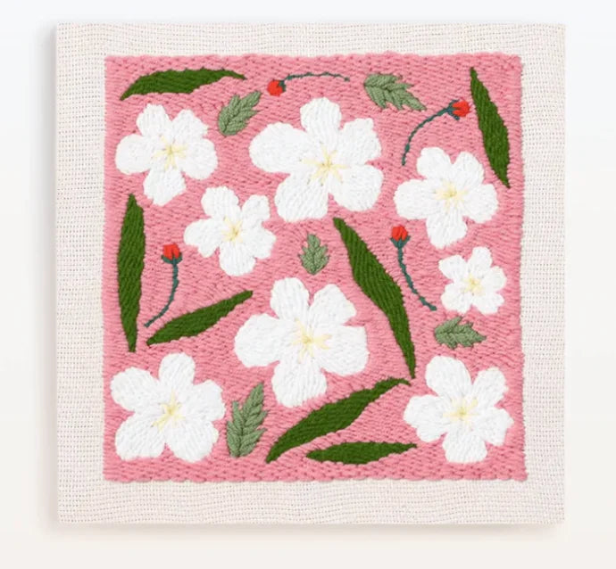 A pink punch needle embroidery featuring white flowers and green leaves.