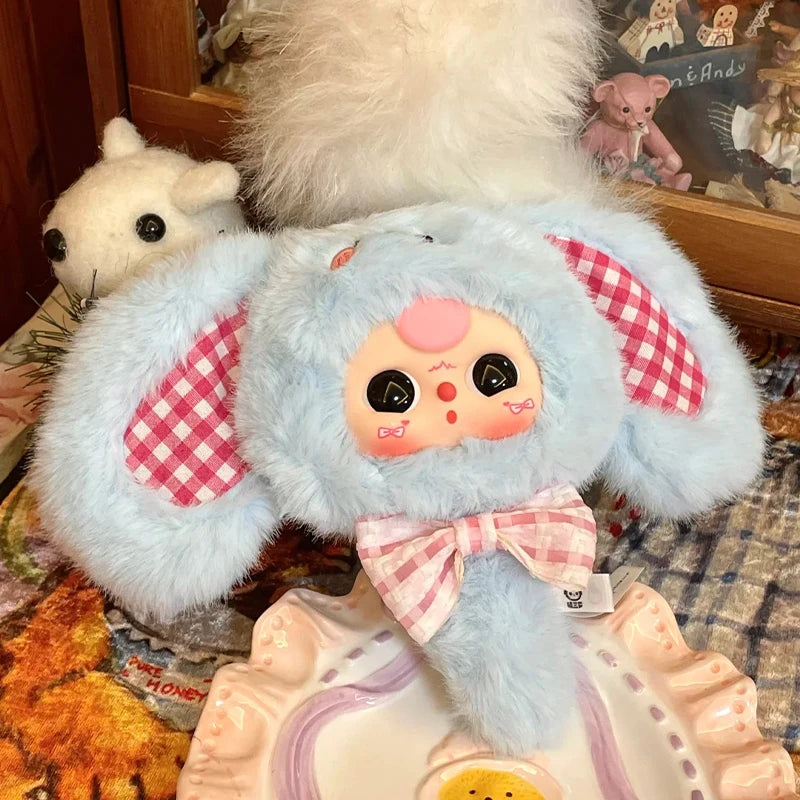 A light blue fluffy blind box figure resembling a baby with pink accents sits on a decorative plate.
