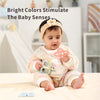 A baby is holding a silicone teether set for babies with a white plush toy in a brightly lit indoor setting.