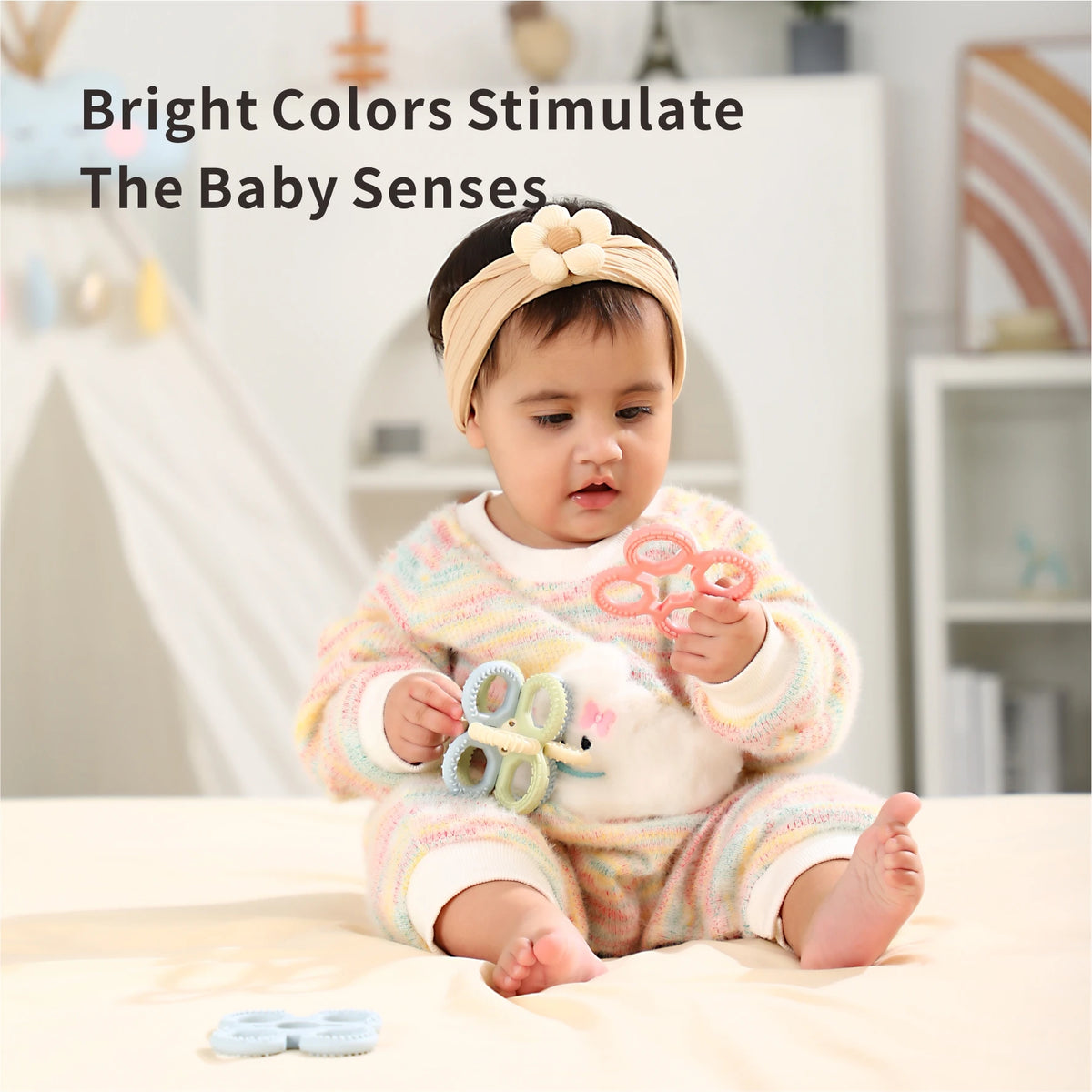 A baby is holding a silicone teether set for babies with a white plush toy in a brightly lit indoor setting.