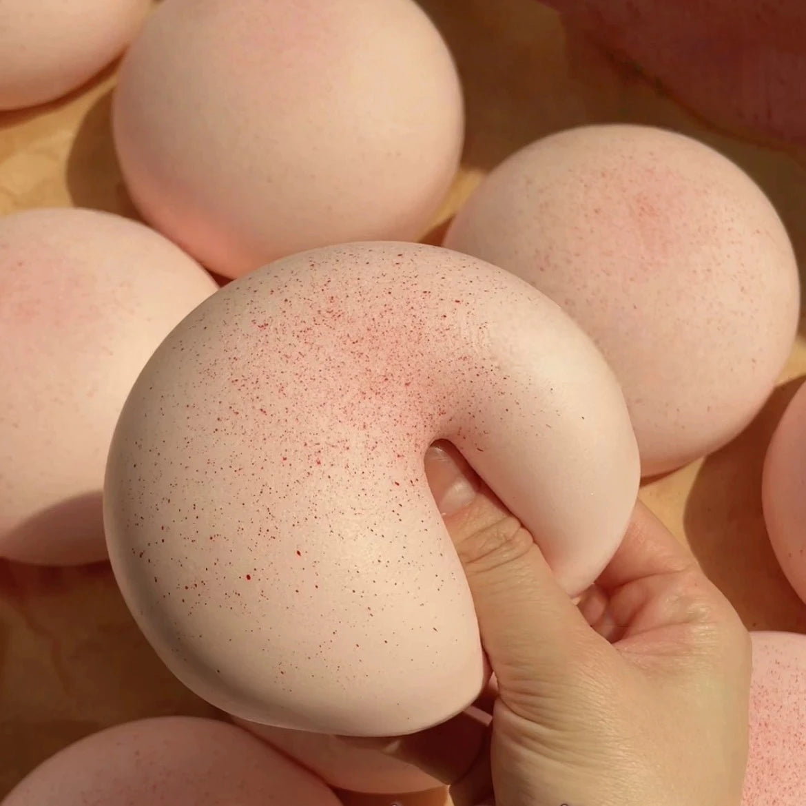 A hand is squeezing a pink, round mochi-shaped squishy stress relief toy against a light wooden surface.