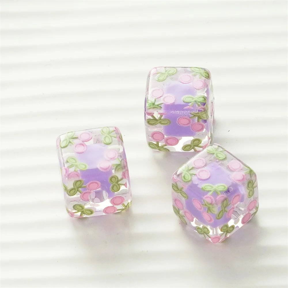 Three square floral resin beads in purple and green hues displayed on a white background.