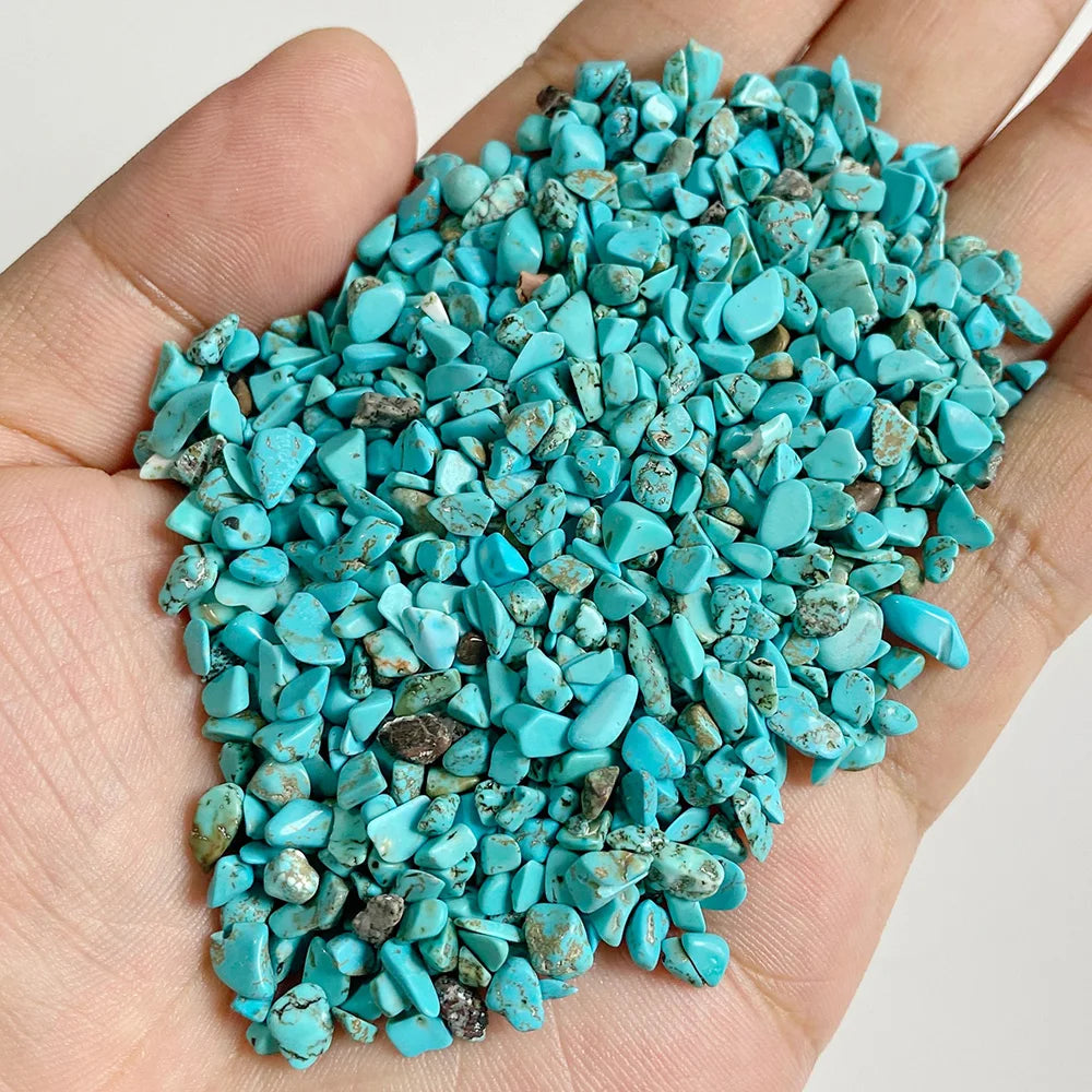 A hand holds a pile of bright turquoise blue natural tumbled stone chips for jewelry making and home decor.