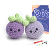 A purple crocheted animal with green leaves is shown next to its packaging and a crochet needle.