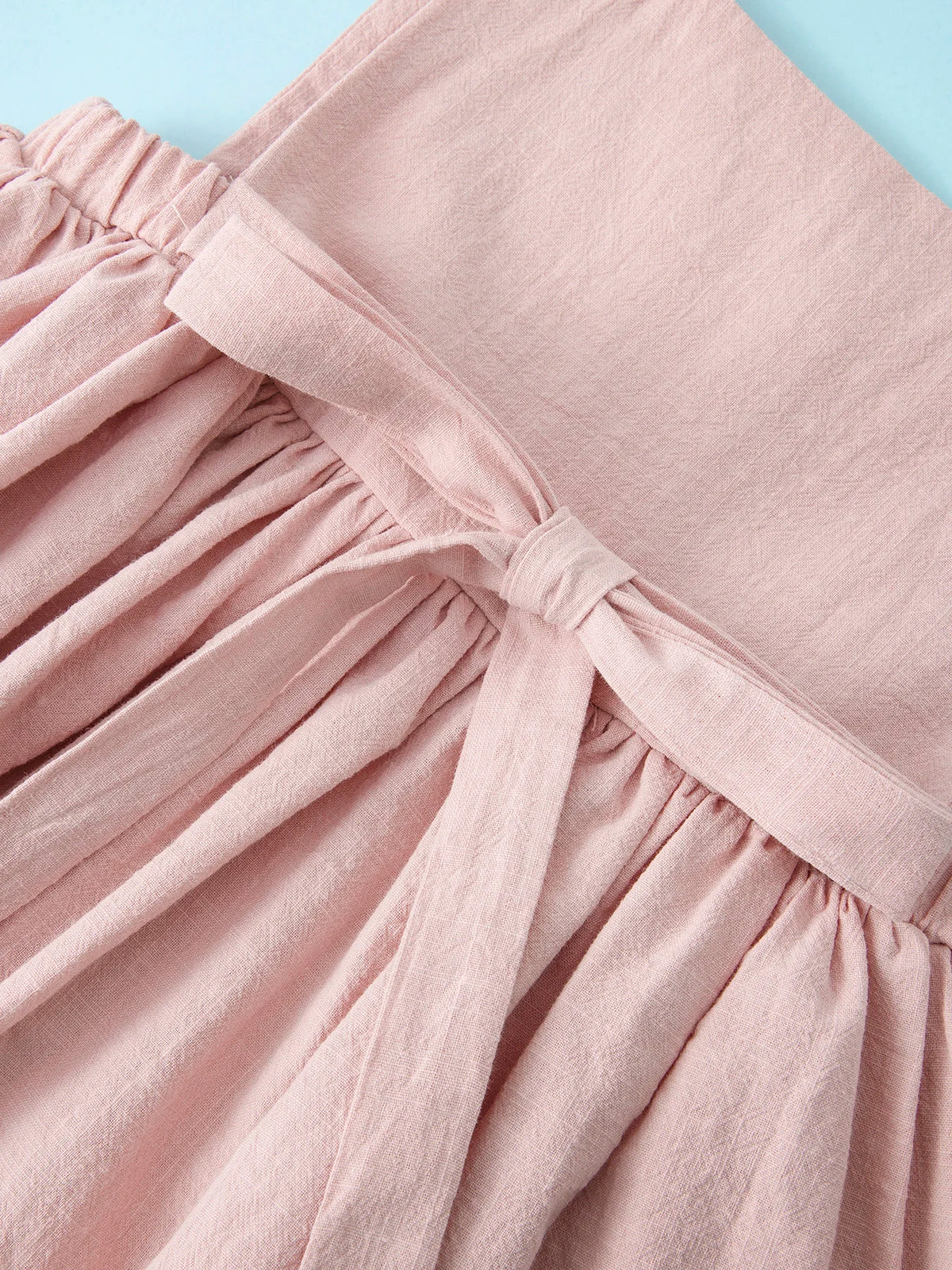 A light pink linen jumper dress for a toddler girl with gathered fabric details.
