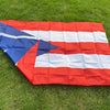 A folded Puerto Rico national flag made of red, white, and blue fabric lying on green grass.