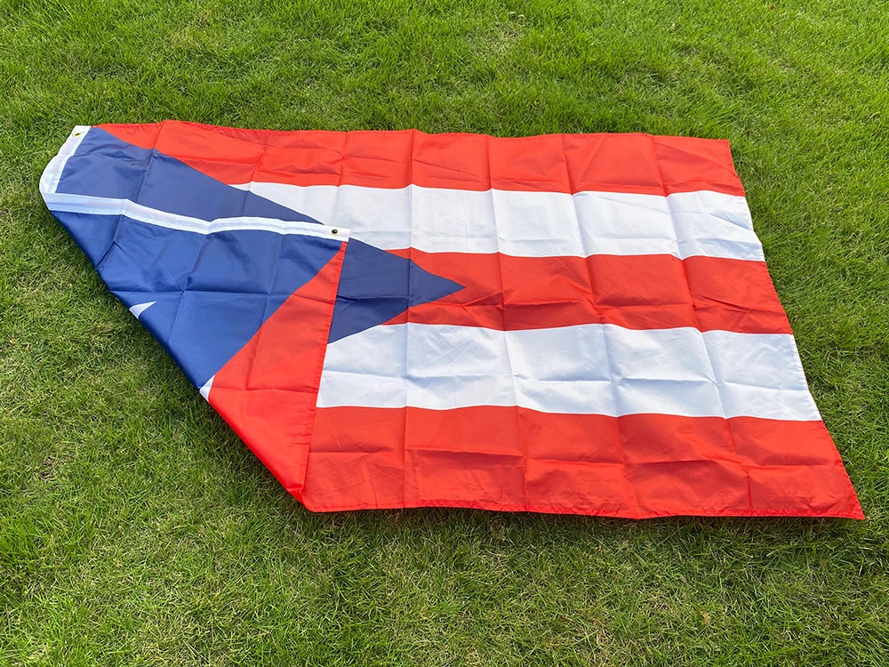 A folded Puerto Rico national flag made of red, white, and blue fabric lying on green grass.