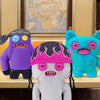 A collection of three plush toys resembling ugly monsters with human-like teeth, featuring purple, blue, and white skin tones