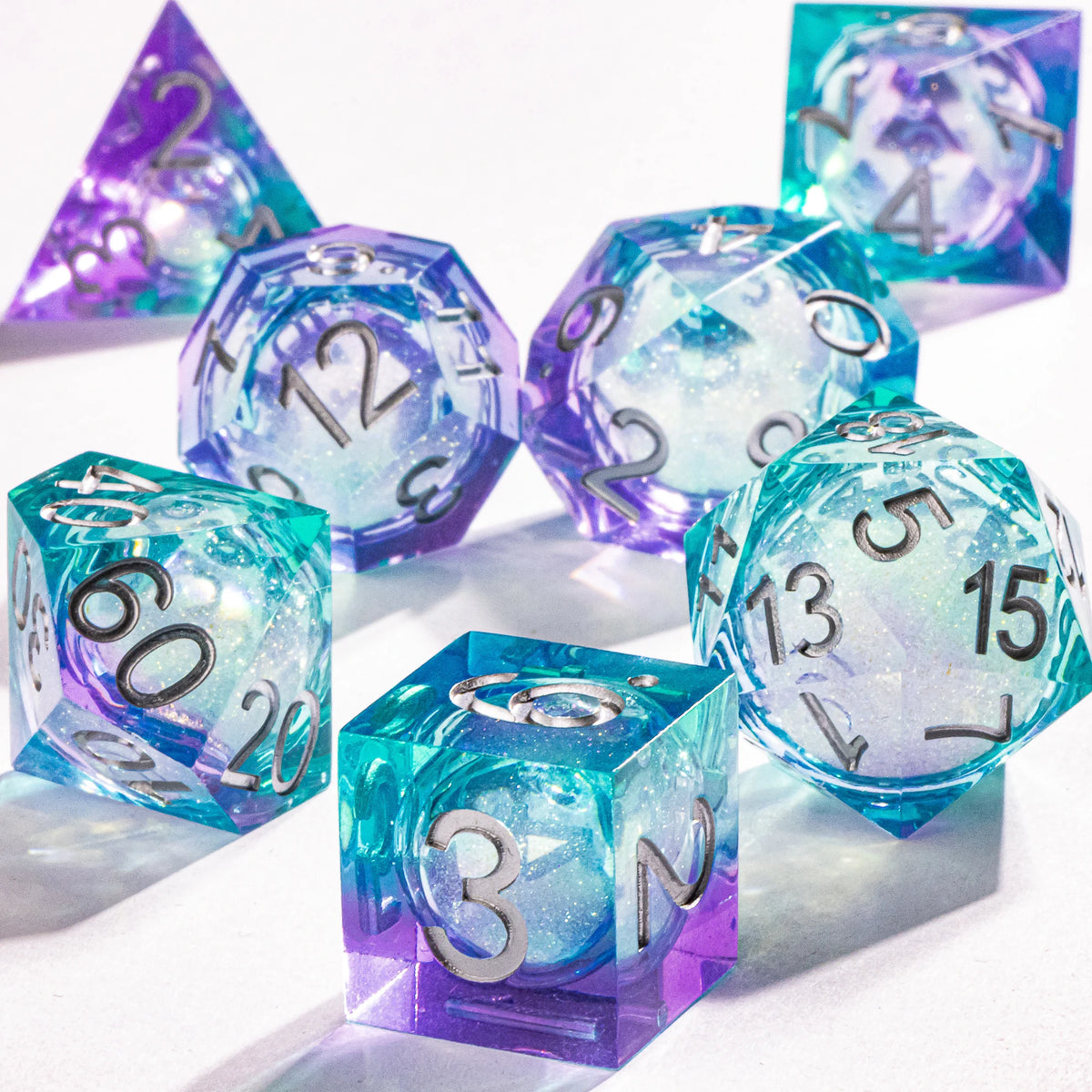 A collection of handmade liquid core polyhedral dice in shades of purple and blue with a galaxy finish