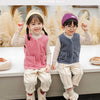 Two children wearing light pink and blue wool vests with white pants and boots