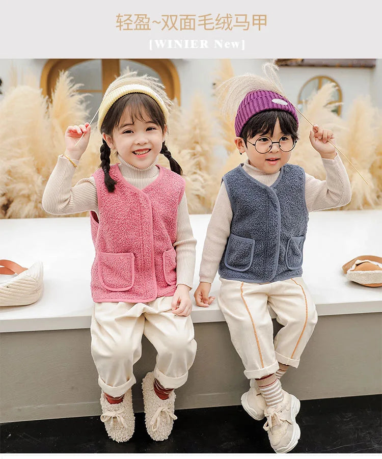 Two children wearing light pink and blue wool vests with white pants and boots