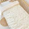 A white fleece blanket with small gold crescent moon patterns is draped over a wooden crib railing.