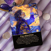 A dark blue oracle card featuring a portrait of a man with flowing hair and blue clothing against an orange and yellow backgr