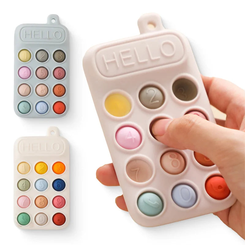 A hand holds a pink silicone baby teether toy with multiple colored silicone rings and a hello design.