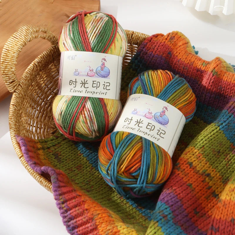 Three skeins of gradient acrylic yarn in various colors are displayed in a woven basket and on a knitted fabric.