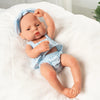 A lifelike vinyl reborn doll with a blue outfit is lying on a white cloth.