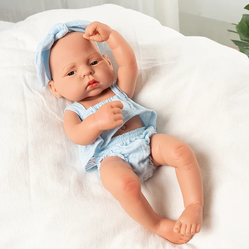 A lifelike vinyl reborn doll with a blue outfit is lying on a white cloth.