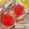 A hand holds a bright red squishy bead stress ball packaged in clear plastic.