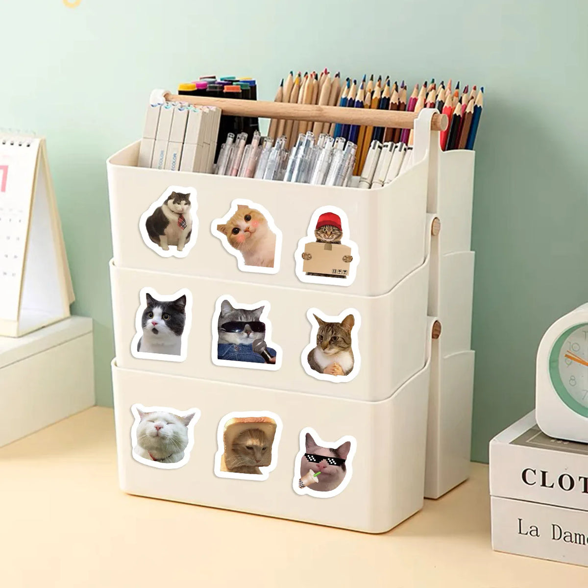 A white storage box filled with pencils and featuring various funny cat meme stickers.