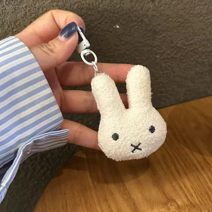 A hand holds a white Miffy cartoon rabbit keychain pendant with a silver clasp against a blurred background.