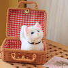 A white plush cat toy with pink ears and a black collar is displayed inside a woven wicker box.