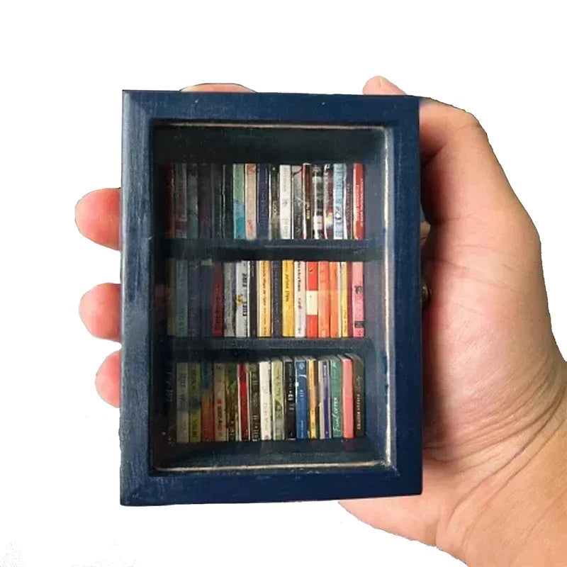 A hand holds a dark blue wooden miniature bookshelf ornament filled with various books.