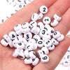 A hand holds a collection of small white and black acrylic number beads for DIY jewelry making