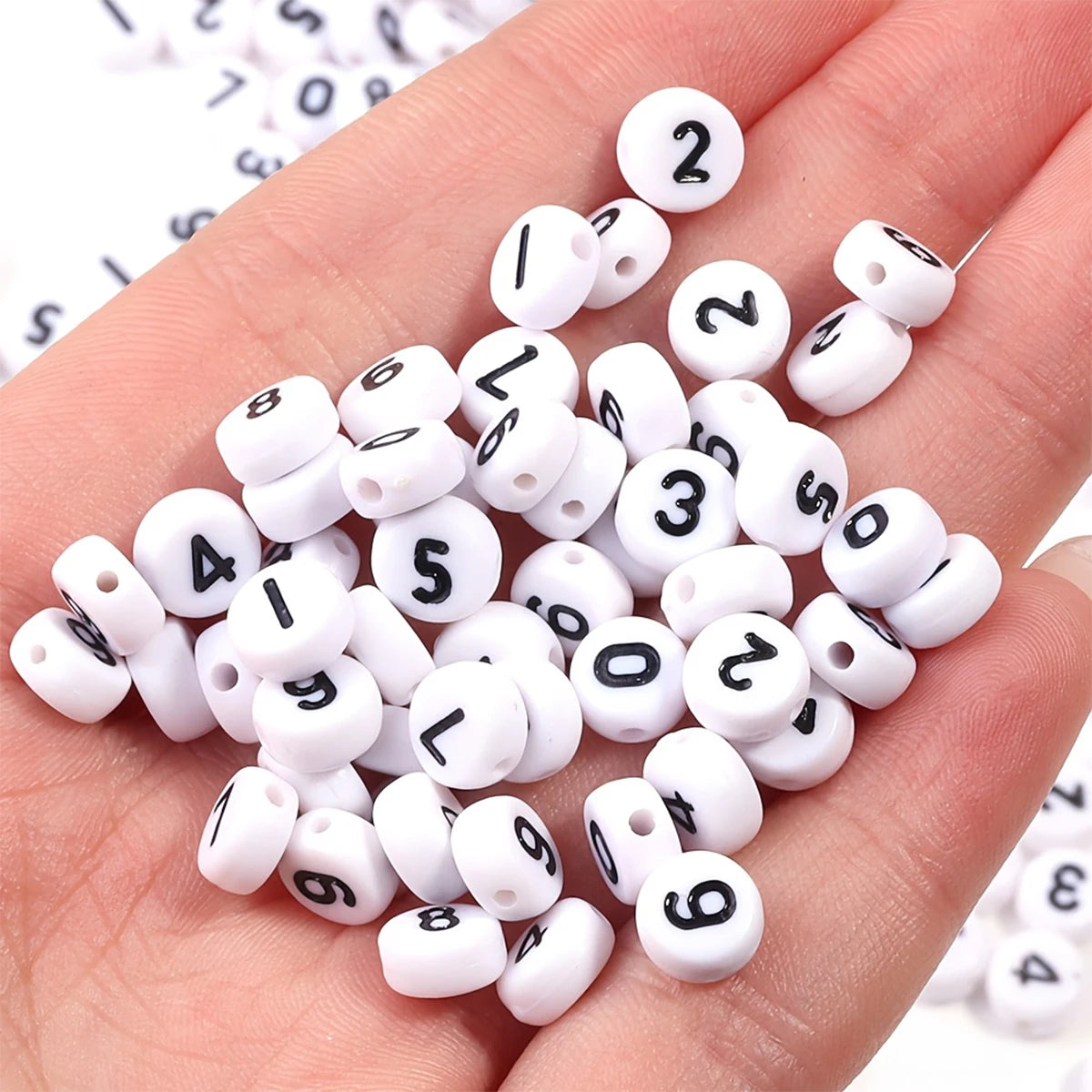A hand holds a collection of small white and black acrylic number beads for DIY jewelry making