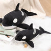 A black and white plush stuffed animal depicting a killer whale and a great white shark resting on a white surface.