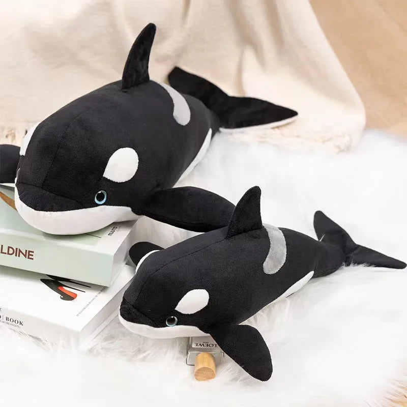 A black and white plush stuffed animal depicting a killer whale and a great white shark resting on a white surface.