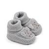 A pair of handmade knitted baby booties in light gray with a textured stitch pattern.