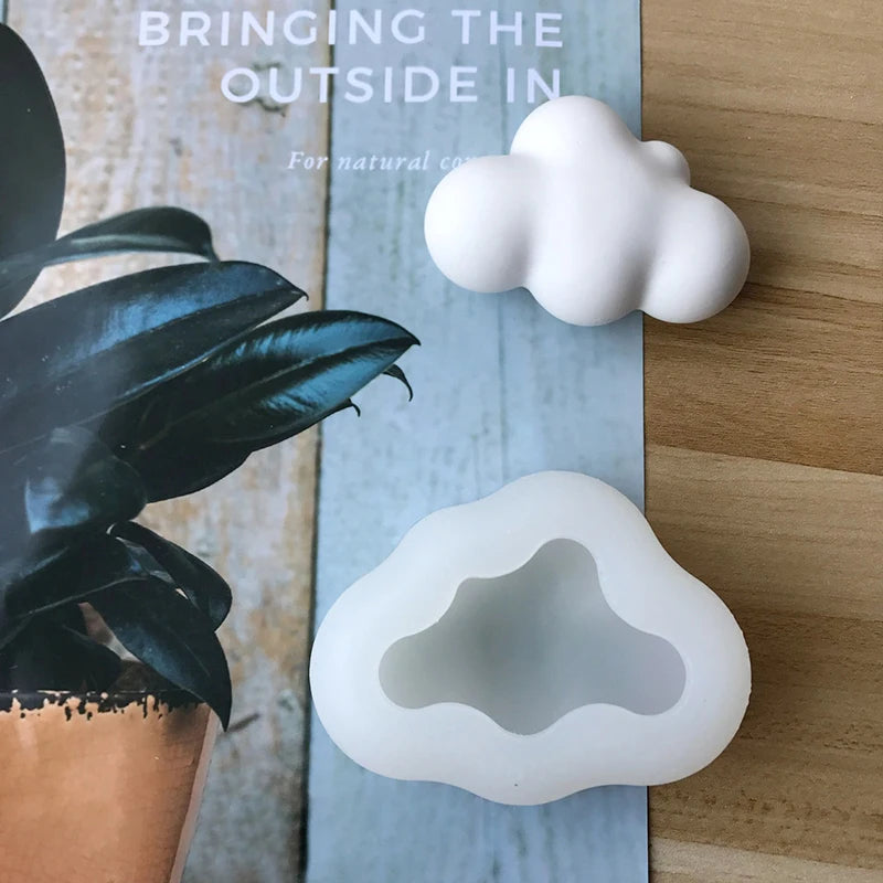 A white cloud-shaped silicone mold rests on a wooden surface next to a dark green plant.