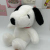 A white plush toy of Snoopy with black ears and a red collar sitting on a white surface.