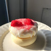 A round, white soufflé with a pink glaze and topped with fresh red raspberries is displayed on a white plate.