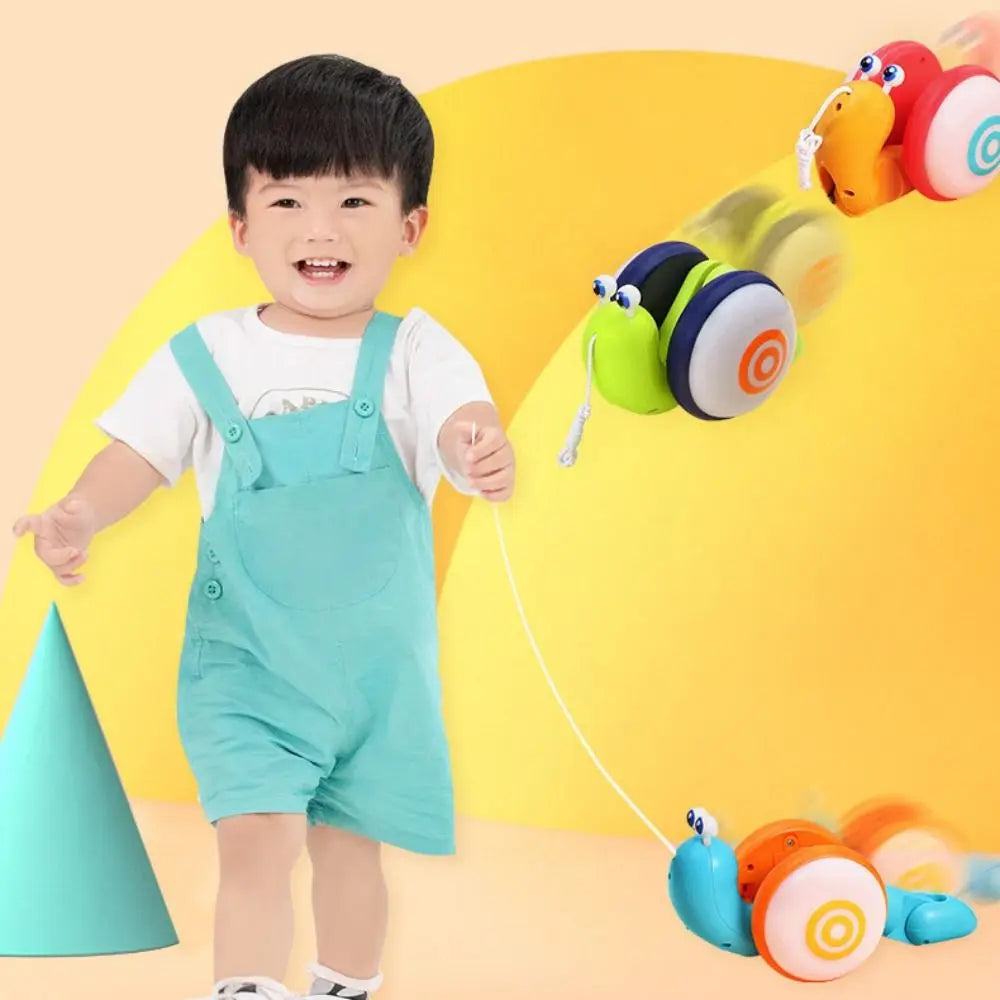 A toddler is playing with a musical pull-along snail toy that is sliding down a yellow surface.