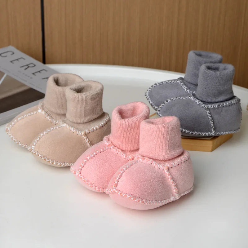 A set of three cozy suede baby booties in pink and gray with plush fur lining displayed on a white surface.