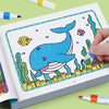 A hand is coloring a blue cartoon whale in a children's coloring book featuring sea life.