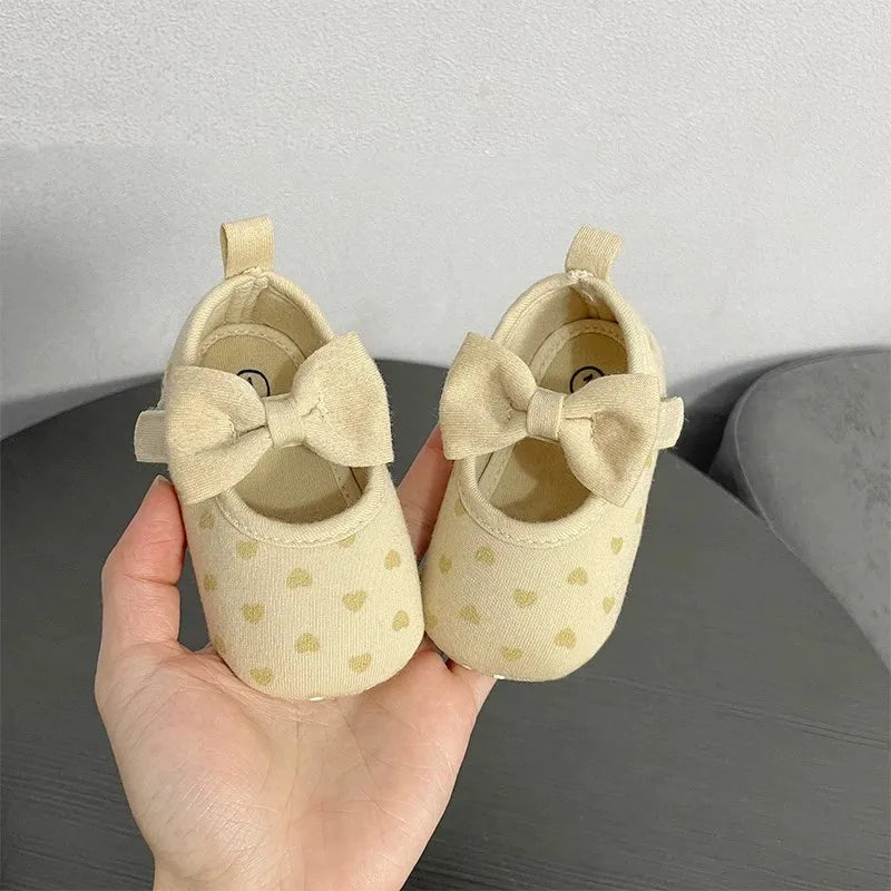 Pair of beige soft sole sandals for baby's first steps featuring a bow detail.