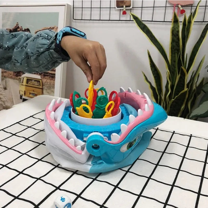 A hand is placing colorful plastic shark teeth pieces into a blue board game tray for family fun.
